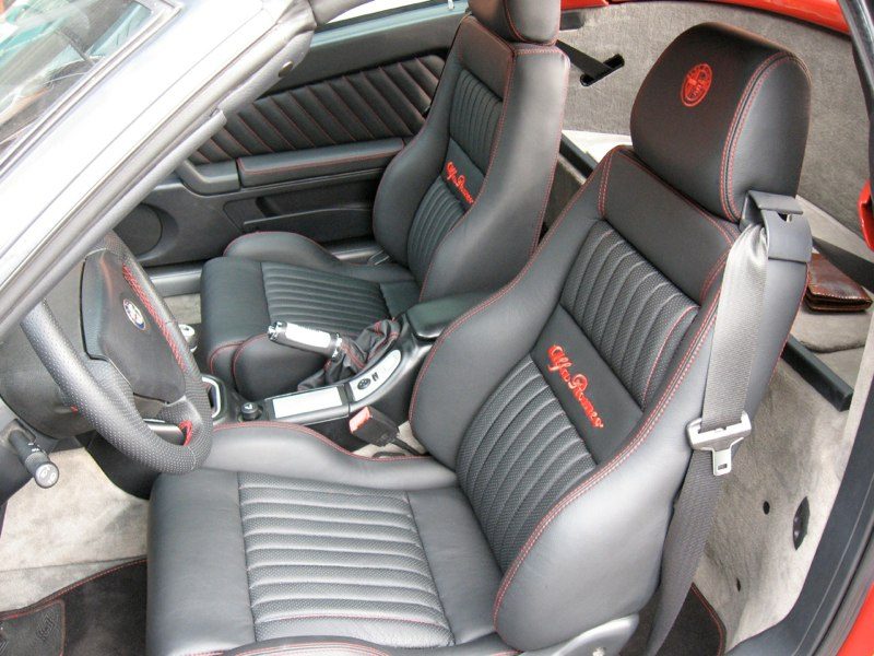 Interni di un'Alfa Romeo GTV rifatti in pelle nera con cuciture rosse a contrasto e logo Alfa Romeo ricamato sullo schienale