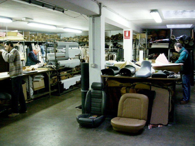Il laboratorio di Artigianauto: scaffali di rotoli di tessuto e pelle, sedili in lavorazione e banchi da taglio